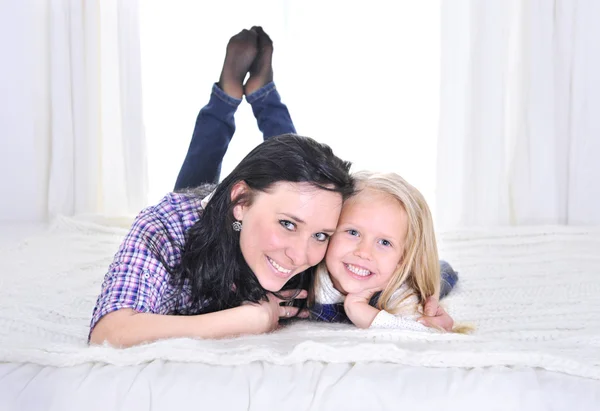 Feliz jovem mãe com bonito pequena filha sorrindo na cama — Fotografia de Stock