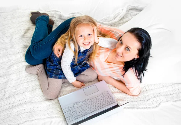 Mãe e filha felizes trabalhando no computador sentados na cama juntos — Fotografia de Stock