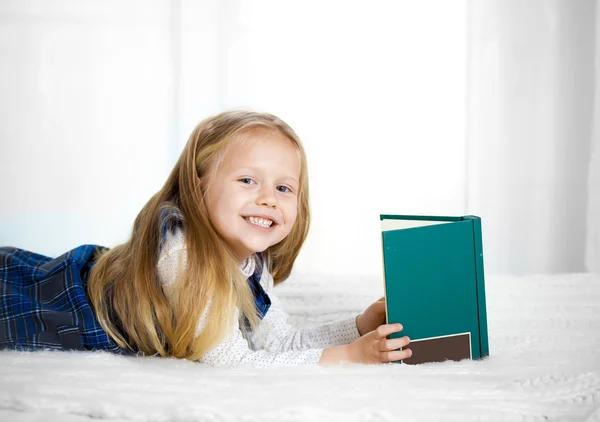 Feliz bonito loira cabelo escola menina lendo um livro olhando para a câmera — Fotografia de Stock