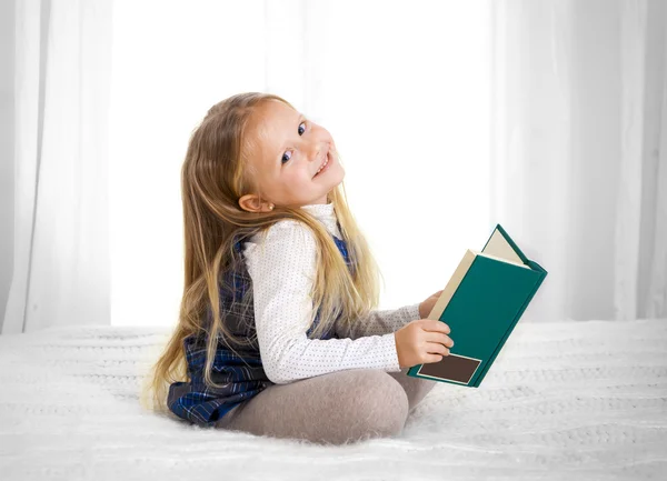 Happy cute blonde haired school girl reading a book on bed sofa — Stock Photo, Image