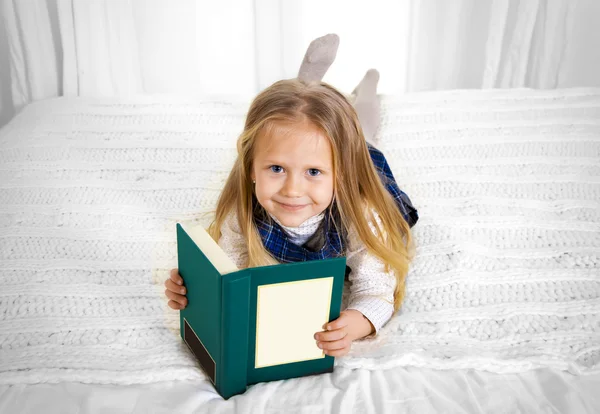 Feliz bonito loira cabelo escola menina lendo um livro deitado na cama — Fotografia de Stock