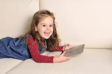 Dijital pad ile oynarken kanepede yatan tatlı küçük kız