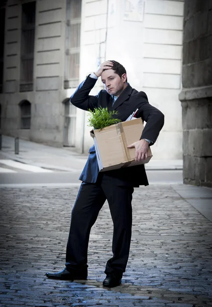 Frustrated business man on edgy street fired from job  carrying cardboard box looking desperate and in stress — Stock Photo, Image