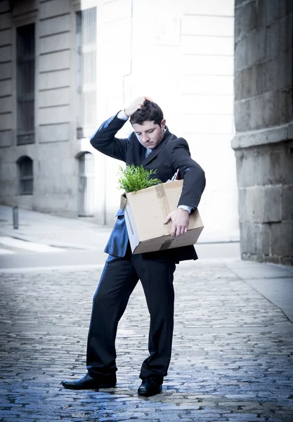 Frustrated business man on edgy street fired from job  carrying cardboard box looking desperate and in stress — Stock Photo, Image