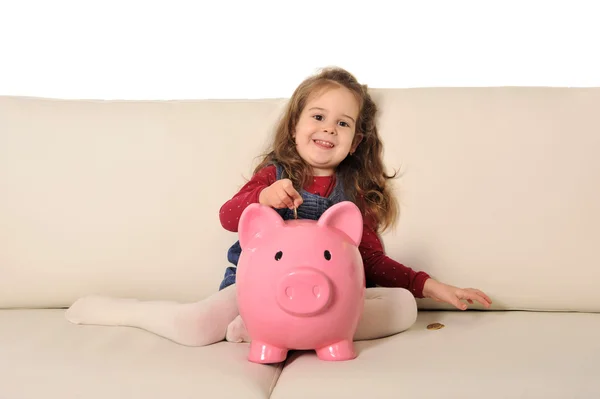 Linda niña jugando pone moneda en enorme alcancía en sofá —  Fotos de Stock