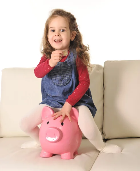 Happy Cute little girl sitting on huge piggy bank inserting Coin — Stock Photo, Image