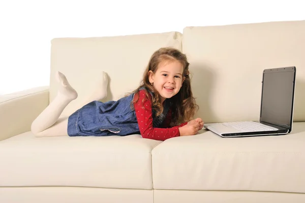 Menina feliz deitada no sofá brincando com o computador — Fotografia de Stock