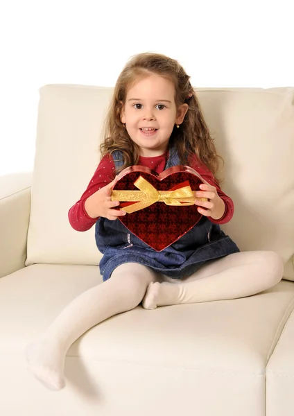 Kleines Mädchen sitzt auf Couch und hält roten Karton in Herzform — Stockfoto