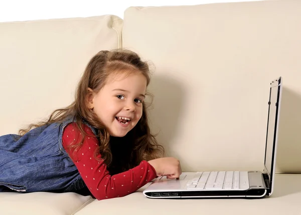 Menina feliz deitada no sofá brincando com o computador — Fotografia de Stock