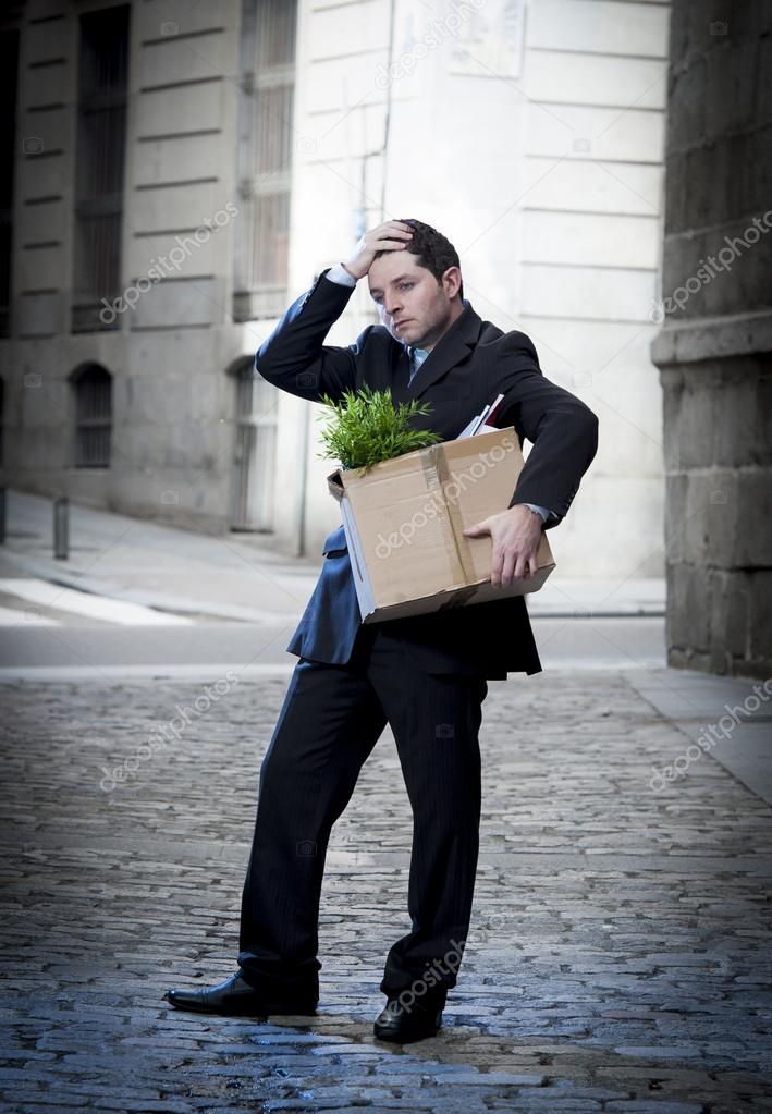 Frustrated business man on edgy street fired from job  carrying cardboard box looking desperate and in stress