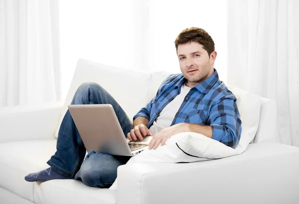 Attraktiver Mann, der zu Hause auf der Couch mit dem Computer arbeitet — Stockfoto