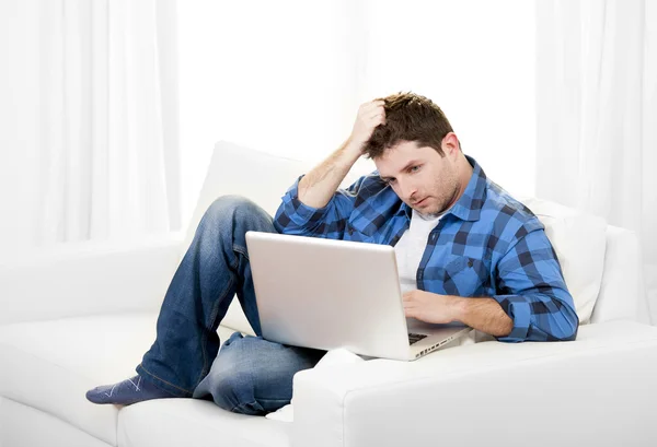 Worried Attractive man with computer sitting on couch — Stock Photo, Image