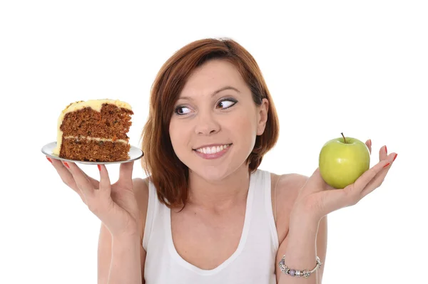 Ung, attraktiv, rødhåret kvinne med eple og kake i hendene i friskt mot junk food dessertvalg isolert på hvit bakgrunn – stockfoto