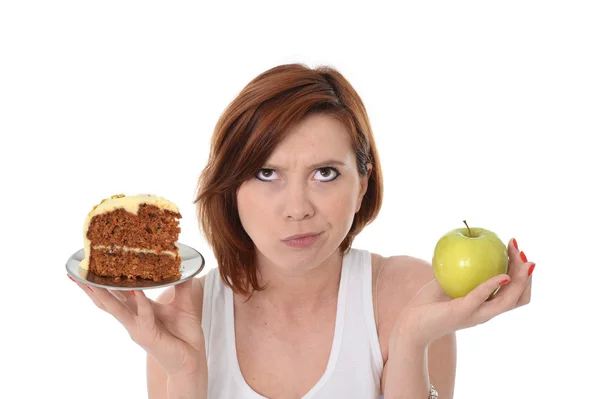 Ung, attraktiv, rødhåret kvinne med eple og kake i hendene i friskt mot junk food dessertvalg isolert på hvit bakgrunn – stockfoto