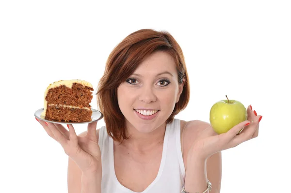 Young attractive sport red hair Woman with Apple and Cake in Hands in healthy versus junk food dessert choice isolated on White background — Stock Photo, Image