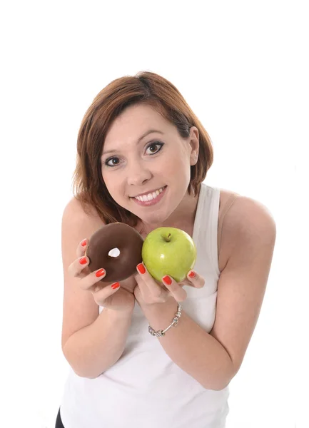 Молодая спортивная женщина с яблоком и шоколадный пончик в руках в здоровой против нездоровой пищи десерт выбор изолированы на белом фоне — стоковое фото