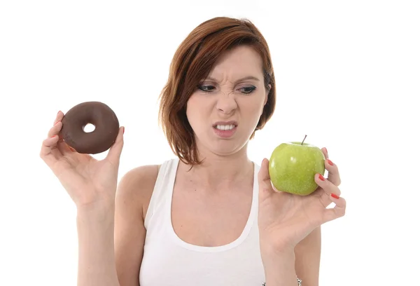 Junge Sportlerin mit Apfel-Schokoladen-Donut in der Hand in gesunder versus Junk-Food-Dessertwahl isoliert auf weißem Hintergrund — Stockfoto
