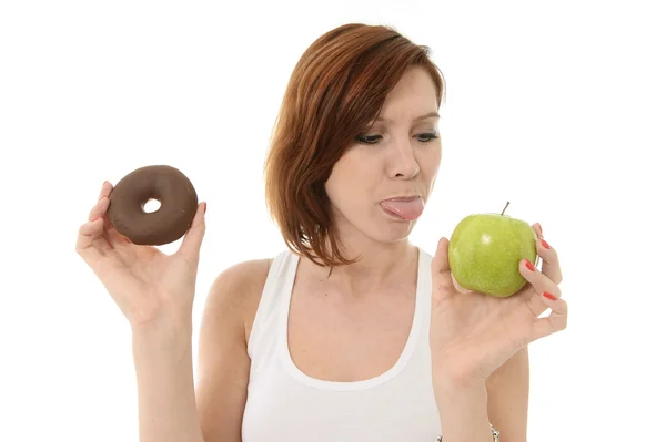 Junge attraktive Frau hält Schokokrapfen mit herausgestreckter Zunge an Apfel — Stockfoto