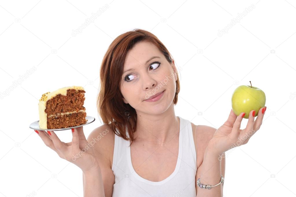 Young attractive sport red hair Woman with Apple and Cake in Hands in healthy versus junk food dessert choice isolated on White background