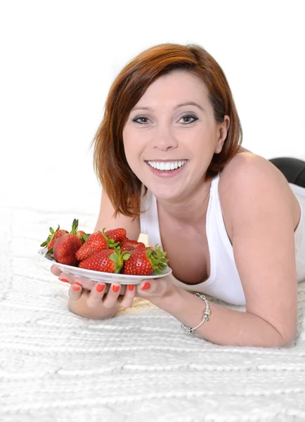 Joven atractiva mujer comiendo un tazón de fresas en la cama —  Fotos de Stock