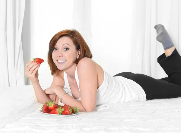 Jovem mulher atraente comendo uma tigela de morangos na cama — Fotografia de Stock