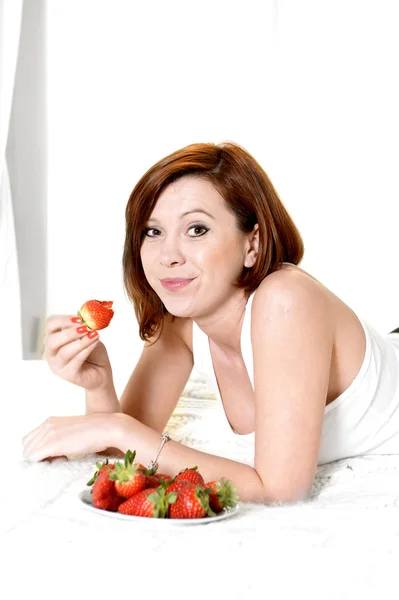 Jonge aantrekkelijke vrouw eten van een kom van aardbeien in bed — Stockfoto