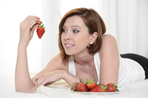 Jonge aantrekkelijke vrouw eten van een kom van aardbeien in bed — Stockfoto