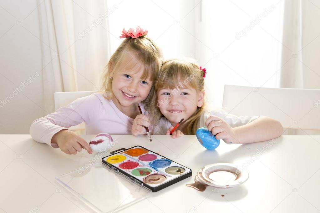 happy blonded girls painting a easter eggs white window 