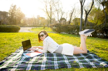 bir parkta dizüstü bilgisayarda çalışan kırmızı saçlı kadın