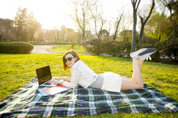 Красивая рыжая женщина работает на ноутбуке в парке — стоковое фото