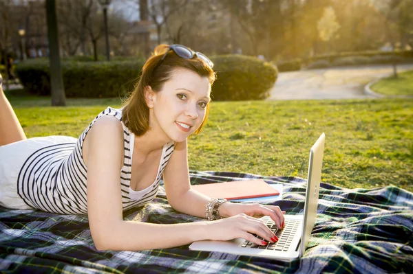 Hübsche rothaarige Frau, die in einem Park am Laptop arbeitet — Stockfoto