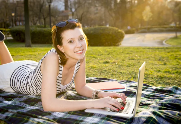 Pretty red haired woman working on laptop in a park — Stock Photo, Image