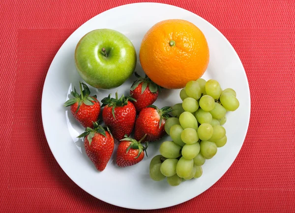 Mix fruits on a plate healthy nutrition concept on red mat — Stock Photo, Image