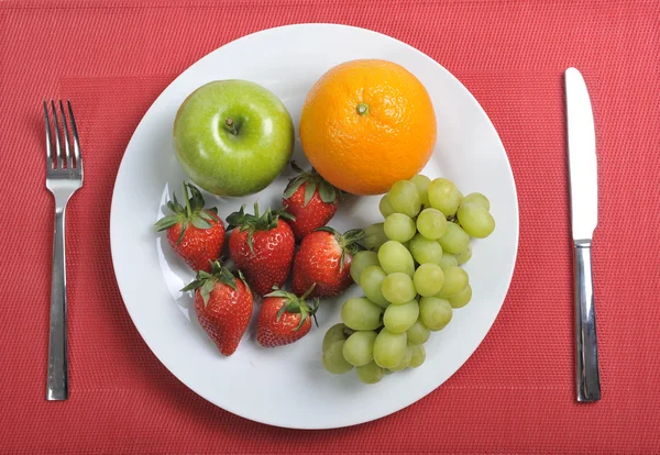 Mix fruits on a plate healthy nutrition concept on red mat — Stock Photo, Image