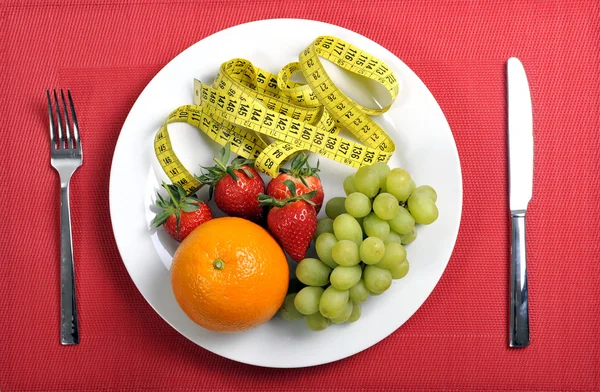 Mix fruits on a plate with measure tape in diet concept on red mat — Stock Photo, Image