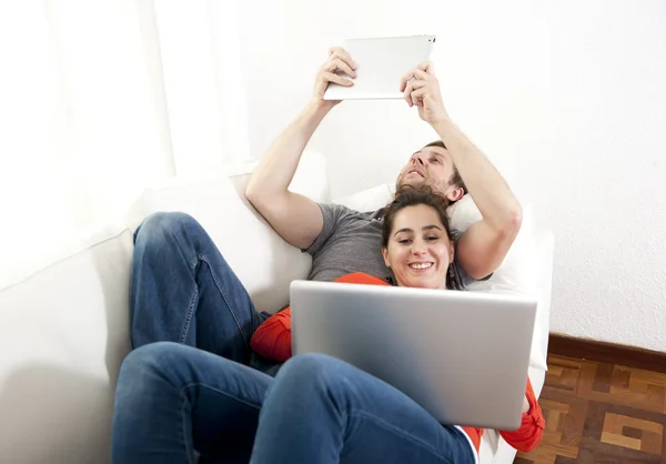 Feliz pareja trabajando en su ordenador portátil y tabletas en un sofá —  Fotos de Stock