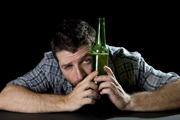 Bêbado homem desperdiçado à mesa com garrafa de cerveja em mãos olhando engraçado — Fotografia de Stock