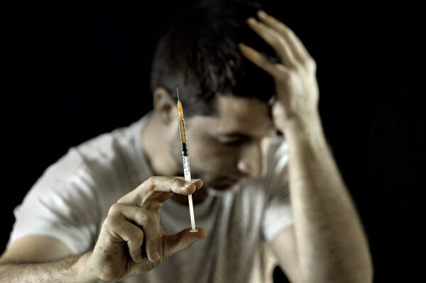 Drug addict man holding heroin or cocaine syringe wasted and depressed