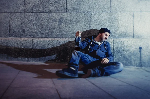 Алкоголик-гранж, сидящий на углу улицы и пьющий бутылку алкоголя — стоковое фото