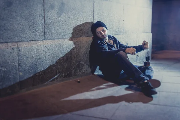 Hombre grunge alcohólico sentado en la esquina de la calle bebiendo botella de alcohol —  Fotos de Stock