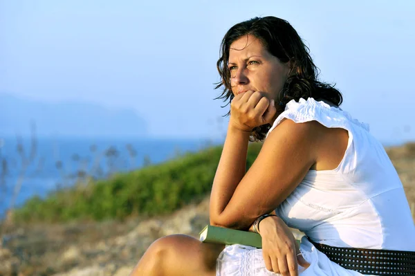 Attractive 40s woman sitting alone on the beach reading a book looking at sea horizon on a relaxing and peaceful summer evening enjoying vacation — Stock Photo, Image