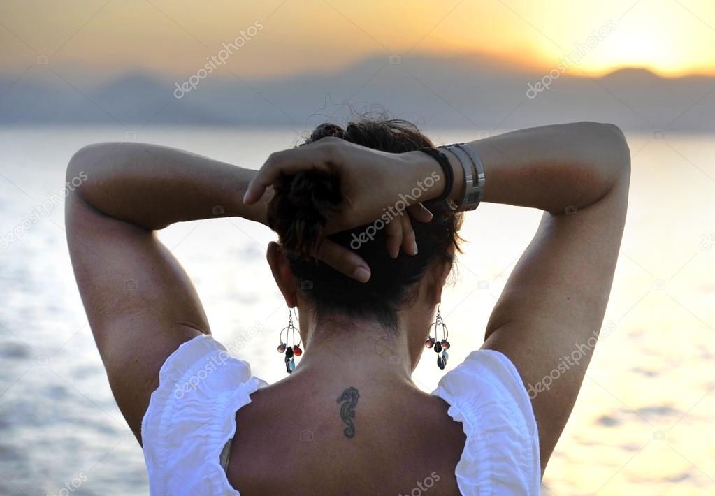 Woman with back seahorse tattoo standing alone looking at sea horizon