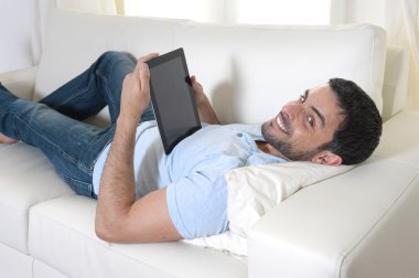 Dijital yüzey veya tablet kanepede oturan kullanan genç mutlu çekici adam