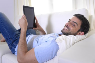 Dijital yüzey veya tablet kanepede oturan kullanan genç mutlu çekici adam