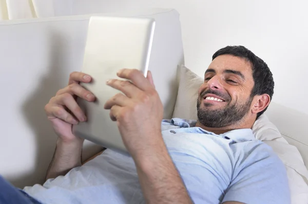 Jovem homem atraente feliz usando almofada digital ou tablet sentado no sofá — Fotografia de Stock