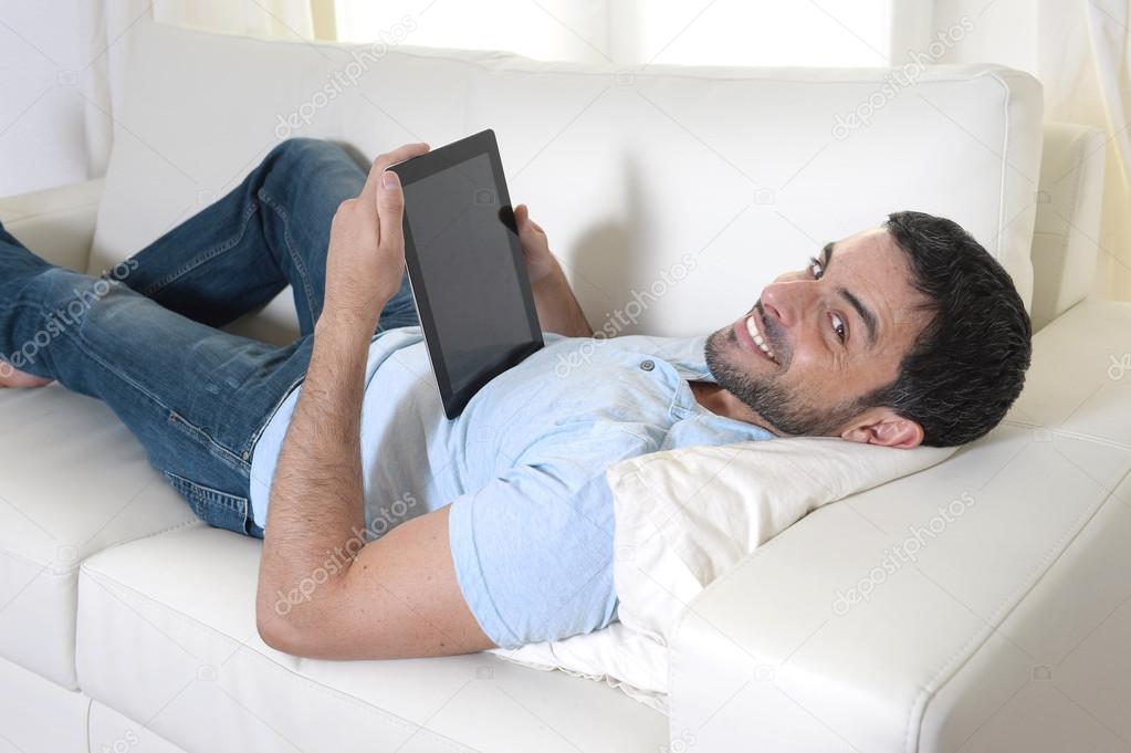 Young happy attractive man using digital pad or tablet sitting on couch