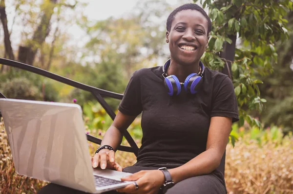 Lachend vrolijk Afrikaans zwart kortharige vrouw studente afro haar met blauwe koptelefoon die online studeert op laptop computer in de zomer groen park. Verscheidenheid. Afstandswerk, afstandsonderwijs. — Stockfoto