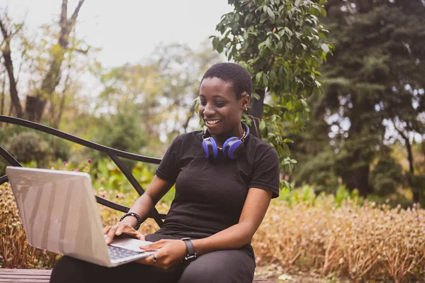 Lachend vrolijk Afrikaans zwart kortharige vrouw studente afro haar met blauwe koptelefoon die online studeert op laptop computer in de zomer groen park. Verscheidenheid. Afstandswerk, afstandsonderwijs. — Stockfoto