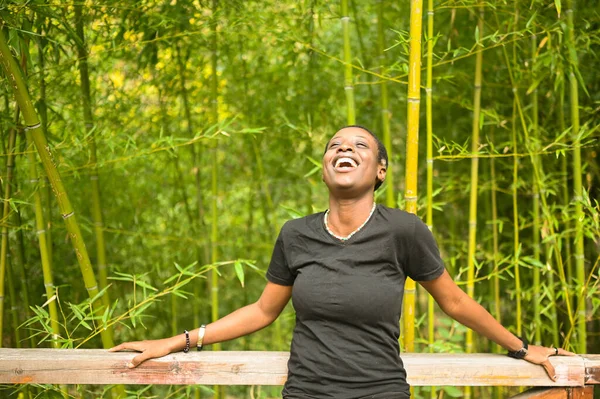 Menarik bahagia tersenyum muda kecantikan alam pendek berambut hitam Afrika wanita tertawa bersandar pada pagar kayu berpose terhadap latar belakang rumpun bambu di taman musim panas alam. — Stok Foto
