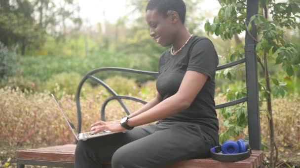 Atractivo feliz elegante africano negro de pelo corto estudiante afro pelo que estudia en línea de trabajo en el ordenador portátil en el parque verde de verano. Diversidad. Trabajo remoto, educación a distancia. — Vídeos de Stock